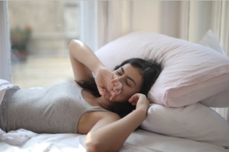 Young woman sitting on a bed, yawning, showing signs of fatigue from poor sleep