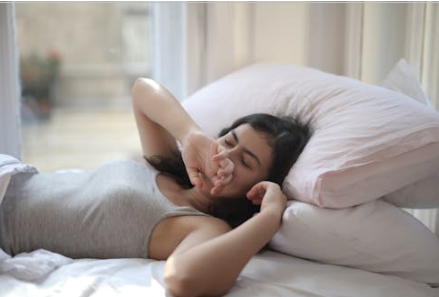 Young woman sitting on a bed, yawning, showing signs of fatigue from poor sleep