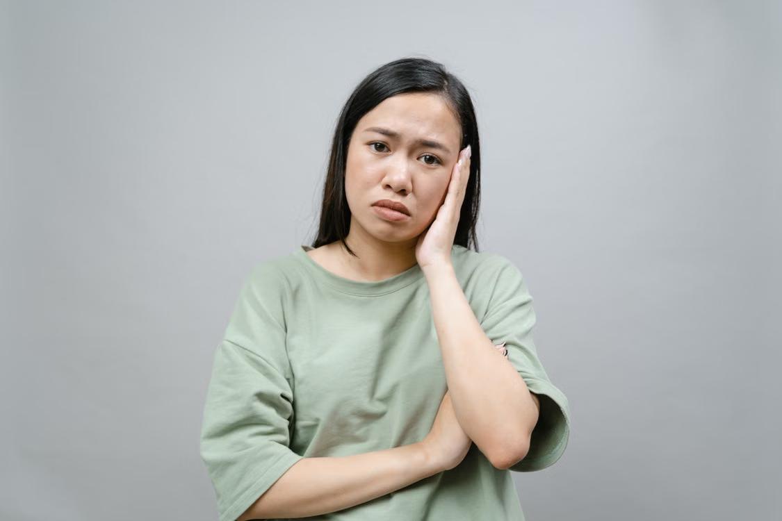 a woman in a green shirt with dental pain.